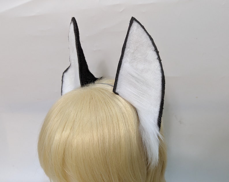 May include: A pair of black and white faux fur cat ears with a black headband. The ears are made of soft, fluffy fur and are attached to a black headband.