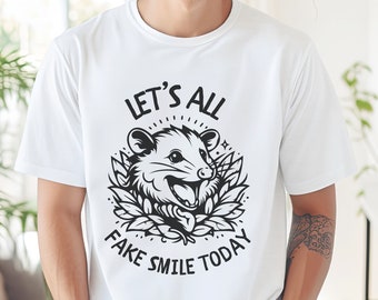 May include: A white t-shirt with a black graphic of a possum with the text "Let's all fake smile today".