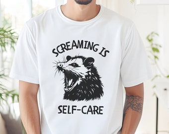May include: White t-shirt with a black and white illustration of a possum with its mouth open and the text "Screaming is Self-Care".