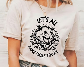 May include: A white t-shirt with a black graphic of a possum with the text "Let's All Fake Smile Today".