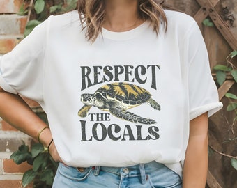 May include: White t-shirt with a vintage-style graphic of a sea turtle and the text "Respect the Locals".