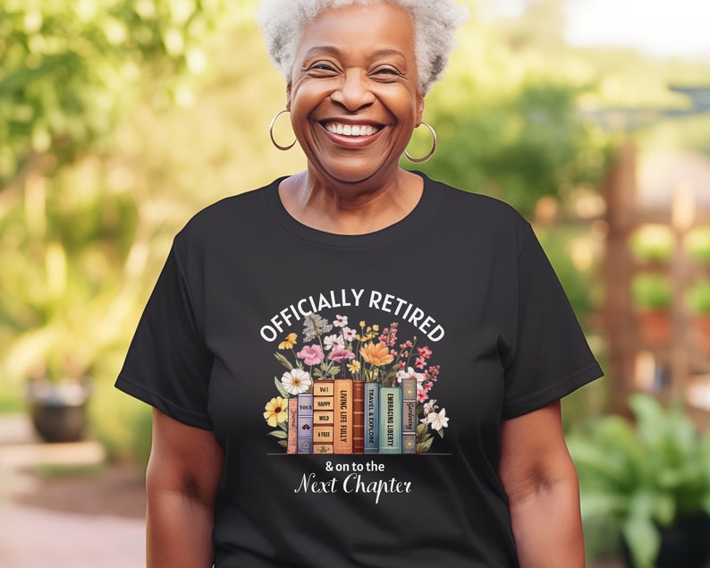 May include: Black t-shirt with white text that reads "Officially Retired & on to the Next Chapter". The text is surrounded by a floral design with a stack of books underneath.