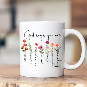 May include: White ceramic mug with a floral design and the text "God says you are" with the words "unique, special, lovely, precious, strong, chosen, forgiven" written vertically down the side.
