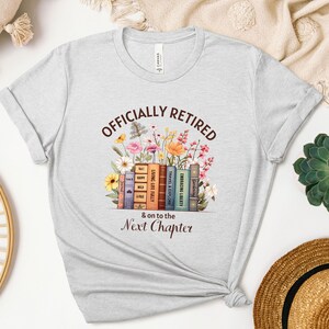 May include: Gray t-shirt with the text "OFFICIALLY RETIRED & on to the Next Chapter" in brown lettering. The text is surrounded by a stack of books with floral illustrations.