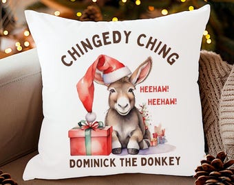 May include: White throw pillow with a cartoon donkey wearing a Santa hat and holding a gift box. The text on the pillow reads "Chingedy Ching Heehaw! Heehaw! Dominick the Donkey".