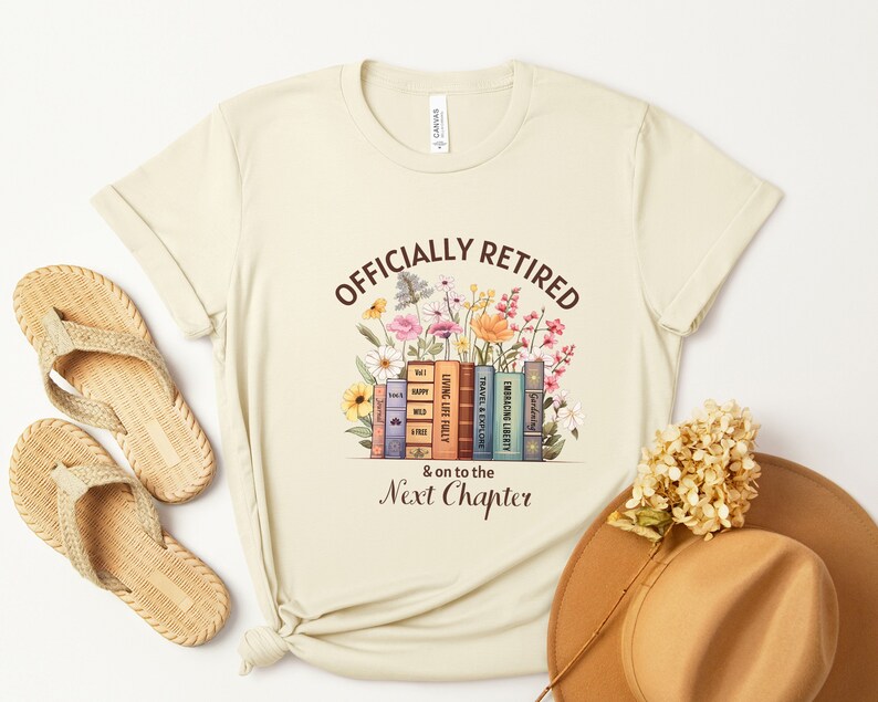 May include: A beige t-shirt with the text "Officially Retired & on to the Next Chapter" printed on it. The text is surrounded by a stack of books with floral illustrations.