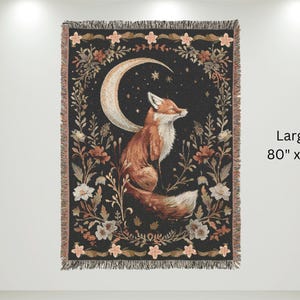 May include: A woven tapestry featuring a fox sitting under a crescent moon with stars. The tapestry has a black background with floral designs in shades of pink, orange, and white. The tapestry is 80 inches by 60 inches.