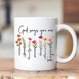 May include: White ceramic mug with a floral design and the text "God says you are" with the words "unique, special, lovely, precious, strong, chosen, forgiven" written vertically next to each flower.