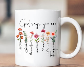 May include: White ceramic mug with a floral design and the text "God says you are" with the words "unique, special, lovely, precious, strong, chosen, forgiven" written vertically next to each flower.