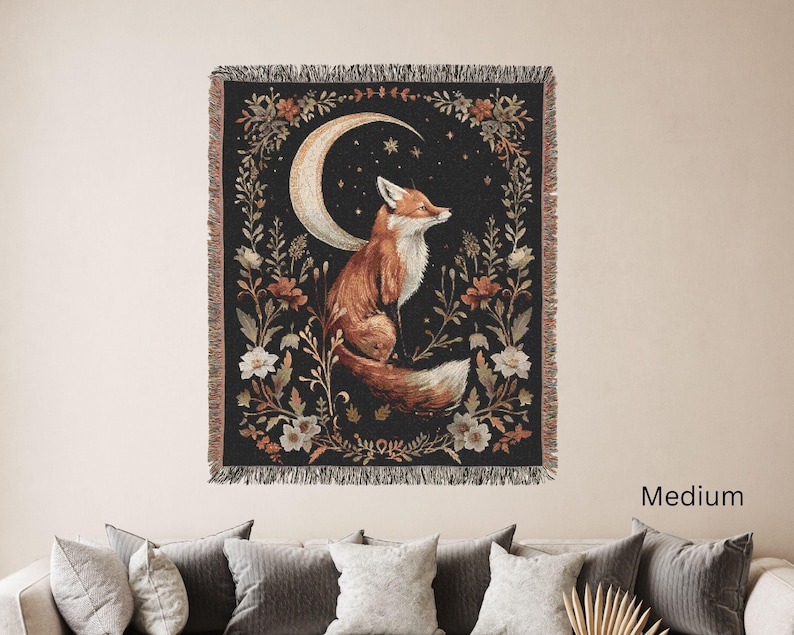 May include: A woven tapestry depicting a fox sitting beneath a crescent moon with stars against a dark blue sky. The fox is surrounded by floral designs in shades of brown, orange, and white. The tapestry has a fringed border.