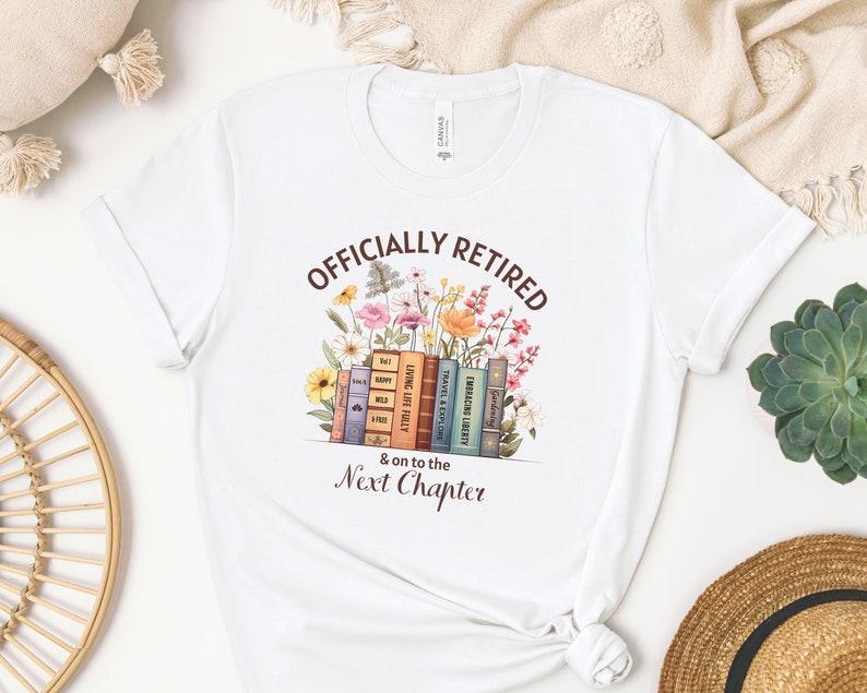 May include: White t-shirt with the text "Officially Retired & on to the Next Chapter" printed in brown. The text is surrounded by a colorful illustration of flowers and books.