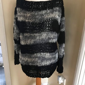 May include: Black and gray striped sweater with a fuzzy texture. The sweater has a loose fit and a boat neck.