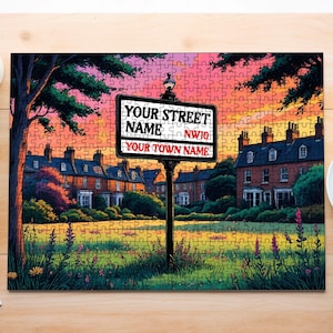May include: A completed jigsaw puzzle featuring a street scene with a sign that reads "YOUR STREET NAME NW10 YOUR TOWN NAME". The artwork depicts a row of houses, a grassy area, and a colorful sunset. A cup of coffee and a plant are on the table.