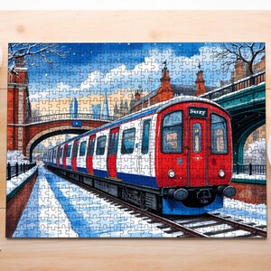 May include: A completed jigsaw puzzle depicting a red, white, and blue London Underground train emerging from a tunnel in a snowy cityscape. The puzzle features a bridge and buildings in the background, with the train tracks in the foreground.