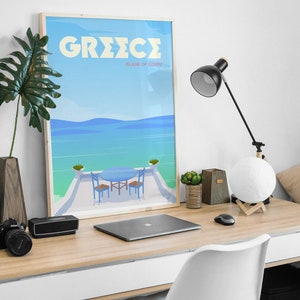 May include: A framed poster with a blue and white illustration of a table and chairs on a balcony overlooking a blue ocean. The poster has the text "GREECE ISLAND OF CORFU" in yellow letters.
