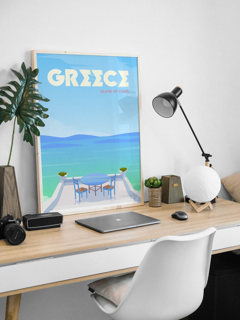 May include: A framed poster with a blue and white illustration of a table and chairs on a balcony overlooking a blue ocean. The poster has the text "GREECE ISLAND OF CORFU" in yellow letters.