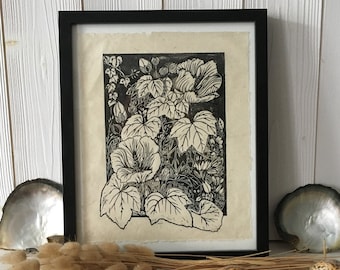 May include: A black and white framed print of a botanical illustration of a flower with large leaves. The print is on a light brown paper and is framed in a black frame.