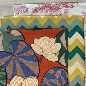 Puede incluir: Tres muestras de tela con diferentes patrones. La muestra superior es blanca con un patrón floral rojo. La muestra del medio es amarilla y verde con un patrón de chevron. La muestra inferior es naranja con un gran patrón floral azul y verde.