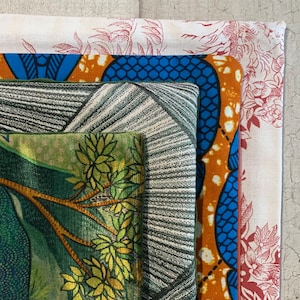 Puede incluir: Un conjunto de cuatro muestras de tela con diferentes patrones. La muestra superior es blanca con un diseño floral rojo. La segunda muestra es azul y naranja con un patrón geométrico. La tercera muestra es gris con un patrón a rayas. La muestra inferior es verde con un patrón de hojas.