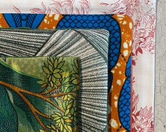 Puede incluir: Un conjunto de cuatro muestras de tela con diferentes patrones. La muestra superior es blanca con un diseño floral rojo. La segunda muestra es azul y naranja con un patrón geométrico. La tercera muestra es gris con un patrón a rayas. La muestra inferior es verde con un patrón de hojas.