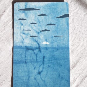 May include: A rectangular tarot card with a blue watercolor design. The card features a sky with cloud shapes and a sun, above a blue sea. The words "10 of swords" are written in cursive at the bottom.