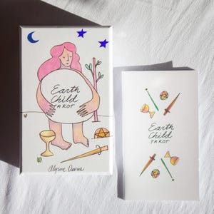 Może przedstawiać: Zestaw kart tarota i pudełko z napisem "Earth Child Tarot". Pudełko przedstawia postać z różowymi włosami i dużą, okrągłą formą. Talia zawiera ilustracje różnych symboli i narzędzi.