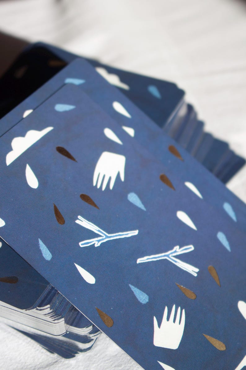May include: A stack of navy blue cards with a repeating pattern of white clouds, raindrops, hands, and twig-like shapes in white and brown. The cards are stacked at an angle, revealing the patterned design.