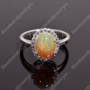 May include: A silver ring featuring a large oval opal gemstone set within a halo of smaller clear gemstones.