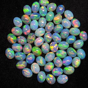 Può includere: Una collezione di pietre preziose di opale di forma ovale e iridescenti. Gli opali sono di colore blu chiaro con bagliori di verde, giallo e rosa.