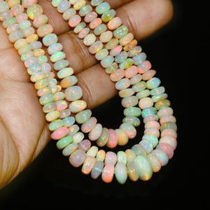 Peut inclure: Gros plan sur des rangées de perles d'opale. Les perles sont de différentes tailles et formes, affichant une gamme de couleurs, dont le blanc, le rose, le jaune et le vert, avec des reflets irisés. Les perles sont enfilées ensemble, créant un collier ou un bracelet.