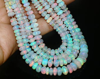 May include: Strands of opalescent opal beads in a variety of sizes. The beads display a range of colors, including white, pink, blue, and green, with a shimmering, iridescent quality. The beads are strung together, creating a necklace or bracelet.