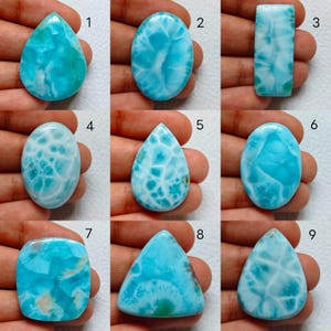 May include: A collection of nine polished Larimar gemstones in various shapes including teardrop, oval, rectangular, and triangular. Each stone displays a vibrant sky-blue color with white, cloud-like patterns and numbered labels from one to nine.