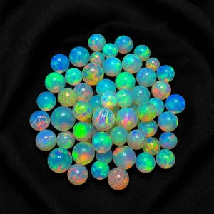 May include: A collection of numerous round, polished opal gemstones. Each stone displays a translucent, milky white base with vibrant flashes of iridescent color, including bright neon green, electric blue, and warm orange fire throughout.