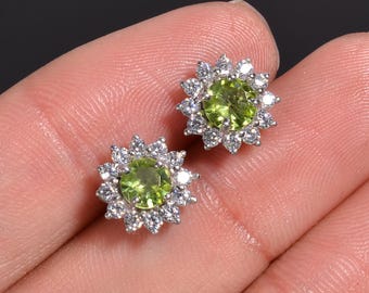 Puede incluir: Un par de pendientes de plata con piedras preciosas verdes rodeadas por un halo de piedras preciosas más pequeñas y transparentes.