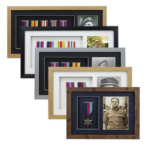 May include: A selection of framed military memorabilia, featuring medals, ribbons, and photographs. The frames are in various colors, including black, grey, and brown, with white or black mounts. The images depict military personnel and awards.