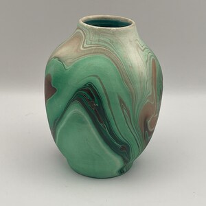 May include: A ceramic vase with a marbled design. The vase features a blend of green, brown, and cream colors. The swirling pattern creates a unique aesthetic. The vase has a wide body and a narrow neck, suitable for displaying flowers or as a decorative piece.