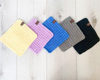 May include: Five crocheted dishcloths in different colors: yellow, purple, blue, gray, and black. Each dishcloth has a small brown tag with the word "Studio" on it.