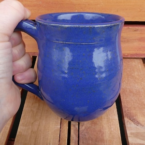 May include: A blue ceramic mug with a rounded body and a handle. The mug has a speckled glaze and a slightly uneven rim.