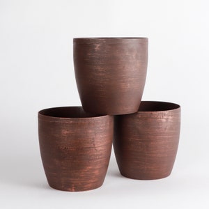 May include: Three brown terracotta-colored ceramic planters of different sizes stacked on top of each other. The planters have a rustic, distressed finish.