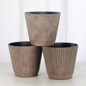 May include: Three brown plastic planters with a textured, ribbed surface. The planters are stacked on top of each other.