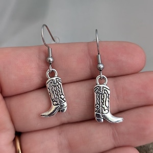 May include: Silver cowboy boot earrings with a detailed design. The earrings have a hook fastening.