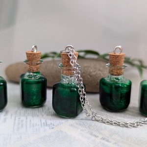 May include: Five small glass bottles with cork stoppers filled with a green liquid. The bottles are attached to a silver chain necklace.