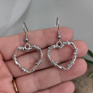 May include: A pair of silver heart-shaped earrings with a barbed wire design.
