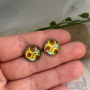May include: A pair of silver stud earrings with a round, blue and yellow sunflower design.