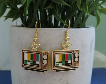 May include: Gold-tone earrings featuring a retro television design with a colourful test pattern on the screen. The earrings have a brown and black finish.