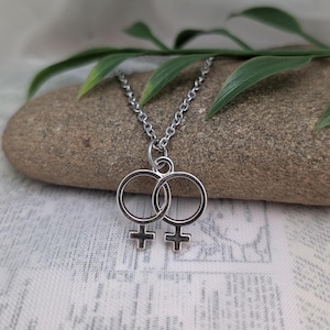 Peut inclure: Un collier en argent avec un pendentif représentant deux symboles féminins entrelacés.