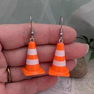 May include: A pair of orange and white traffic cone earrings with silver hooks.