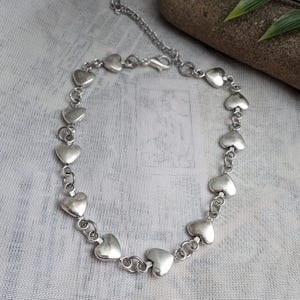 Peut inclure: Un collier en argent avec une chaîne composée de breloques en forme de cœur.