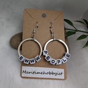 May include: A pair of silver hoop earrings with white letter beads spelling "EWW" and "PEOPLE".