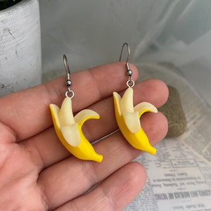 May include: A pair of yellow banana earrings with silver hooks. The bananas are made of polymer clay and have a realistic look.